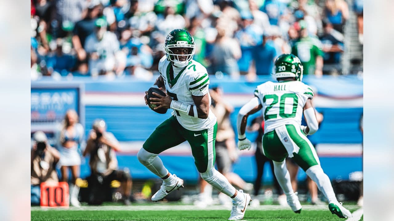 A Jets quarterback in a white number 7 jersey tucks the football and looks downfield while number 20 runs ahead of him in Tennessee.