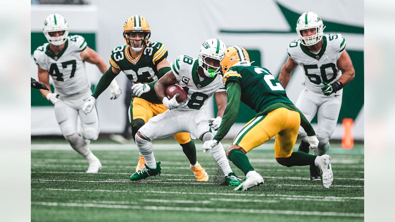 A Jets ball carrier in a white number 8 jersey cuts between two Packers defenders at MetLife Stadium.