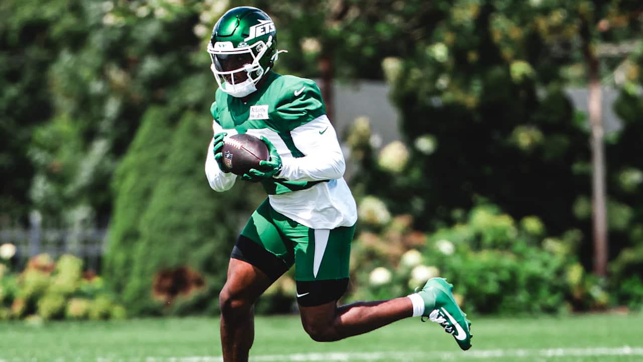 Breece Hall runs with the football in green Jets practice gear.