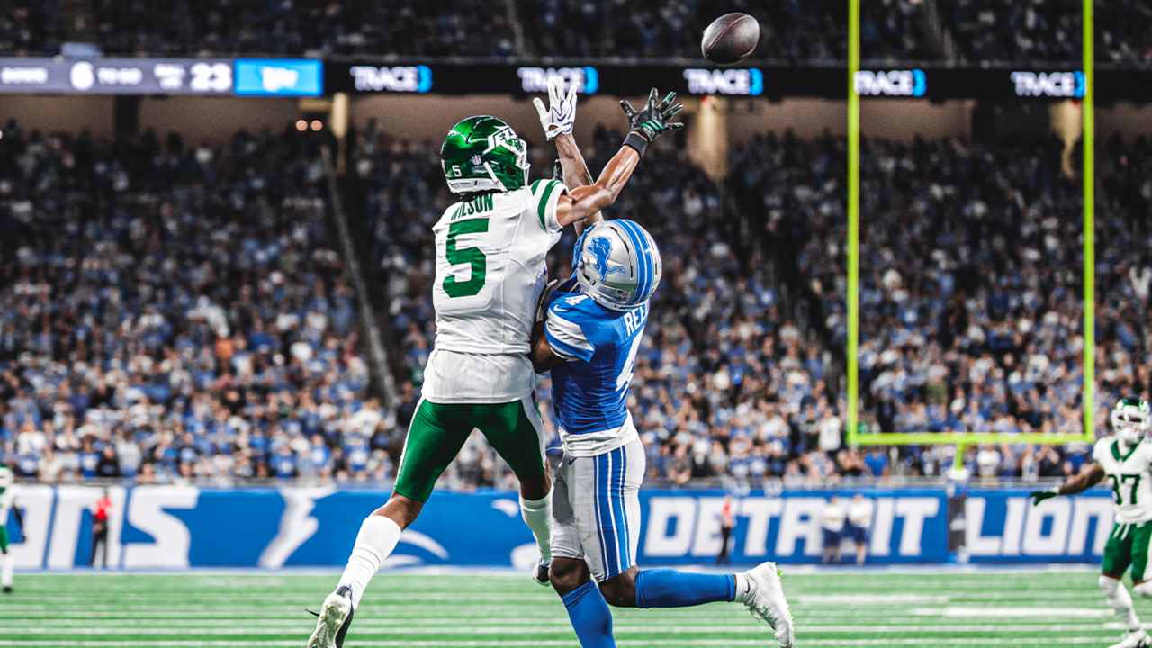 Garrett Wilson reaches for a contested catch with a Detroit defender alongside him.